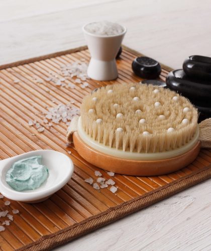Spa treatment, body care and aromatherapy background. Massage brush, zen black stones, aroma salt, herbal balls, other details and accessories for wellness and beauty on bamboo mat with copy space