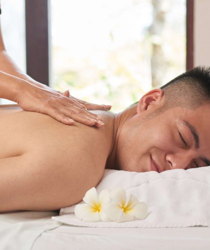 Handsome Asian man with closed eyes getting back massage while lying on treatment table at luxurious spa salon