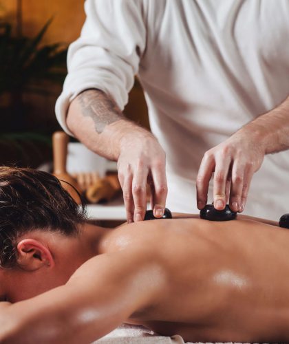 Beautiful young woman getting hot stone massage at spa salon, lying on massage table