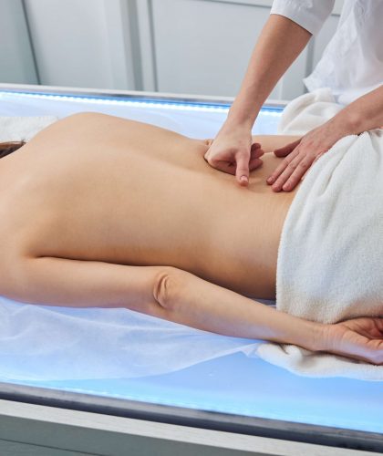 Massage specialist treating the spine on a female with bare torso by putting fist on her back